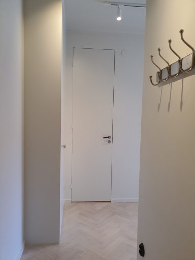 En ljus korridor med en dörr och klädhängare på väggen.