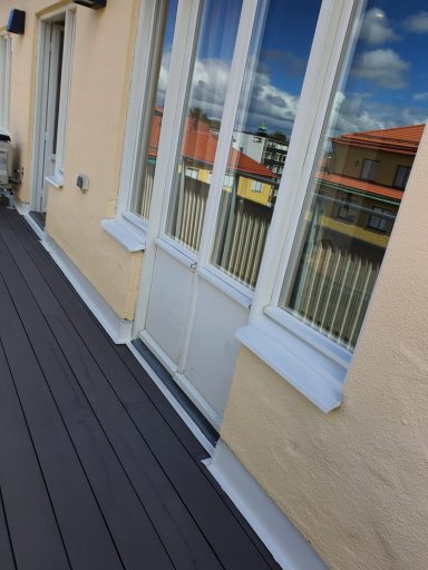 En balkong med glasdörrar och trägolv, med utsikt över en stadsmiljö.