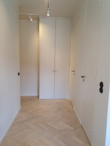 Ljust och sparsamt inrett rum med ljusa väggar och parkettgolv. Två dörrar syns.