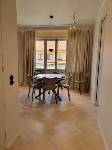 Ljust rum med matbord, stolar och gardiner vid fönster.